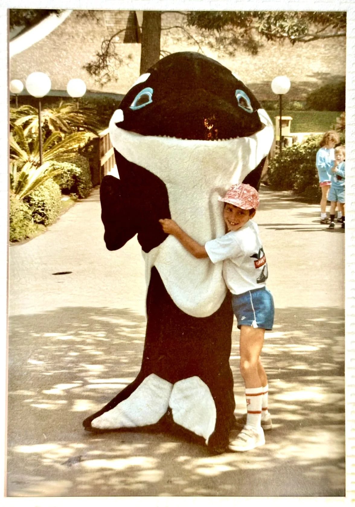 A child in a Save the Whales shirt hugging a costumed orca mascot, 1986.