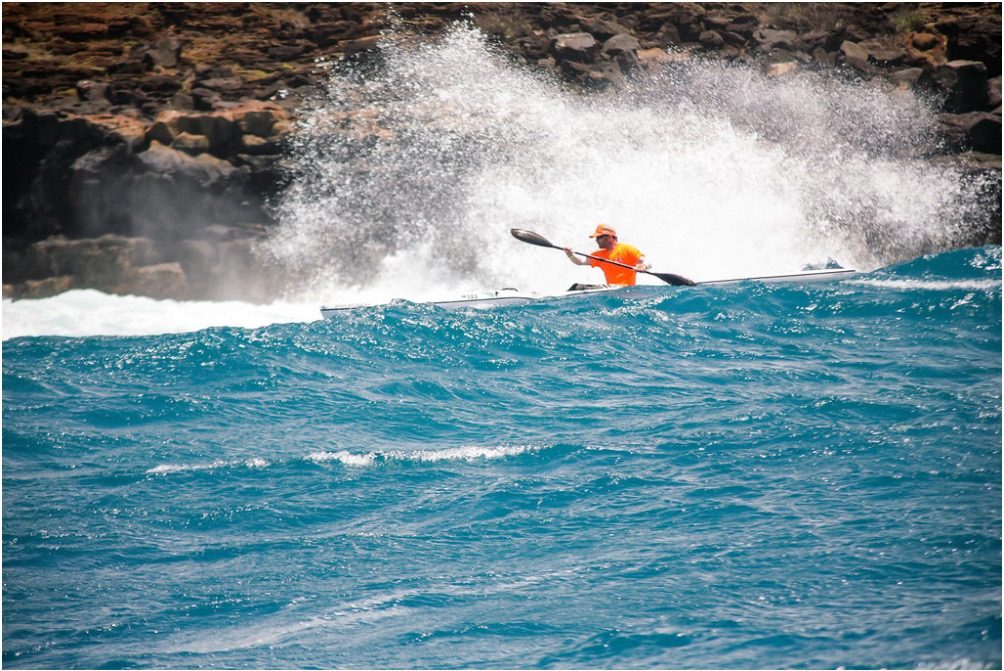 Gabe paddling a surfski down the face of a breaking wave.